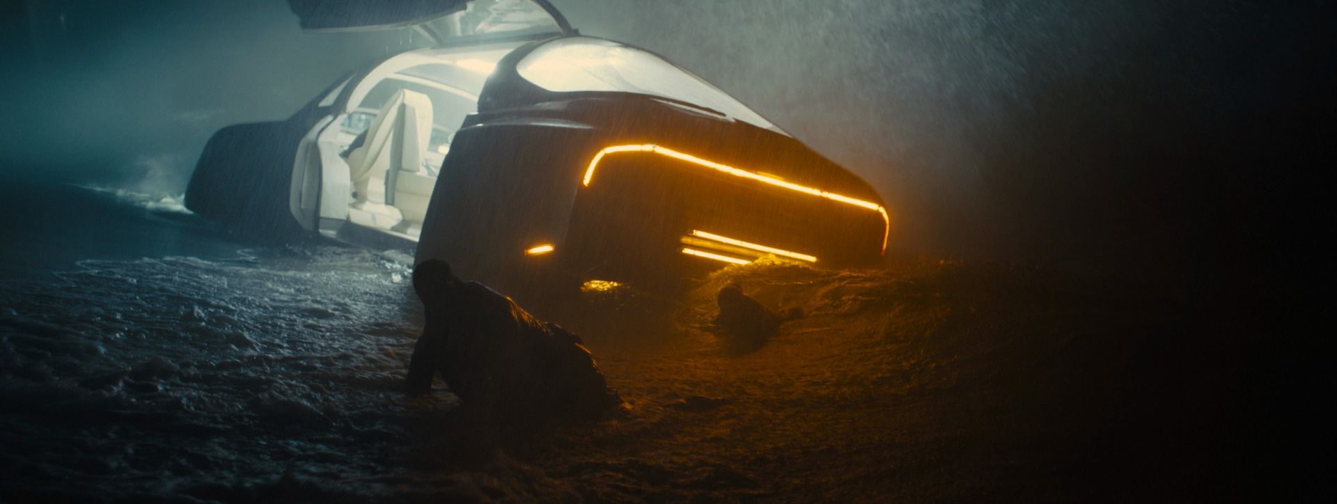 A crashed spinner glows amber in the surf at night as a figure crawls through wet sand, from Blade Runner 2049.