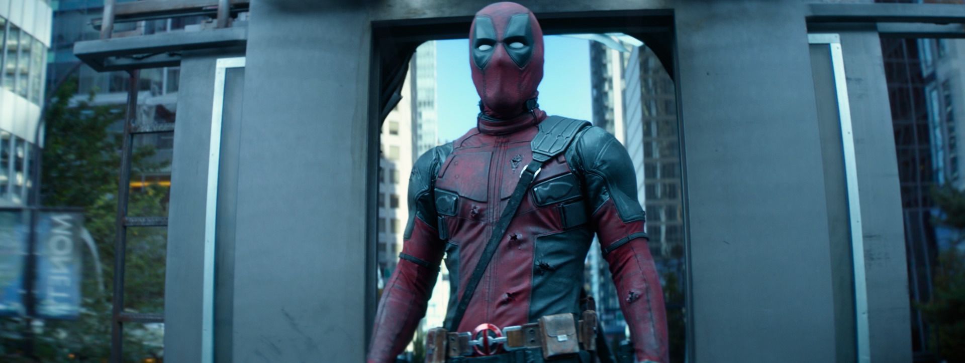 Deadpool stands in a concrete doorway with city towers behind him, from Deadpool 2.